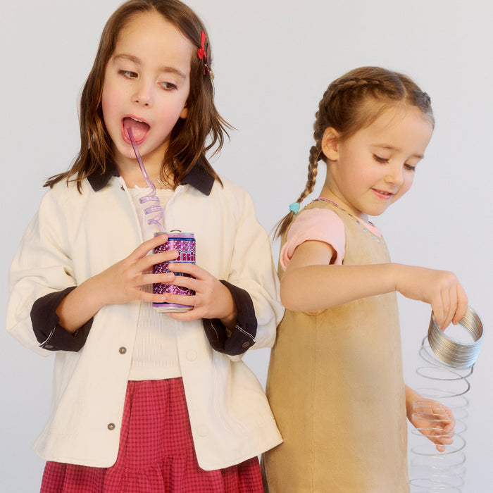 Two young girls in colorful outfits drinking from cups with straws against a white background