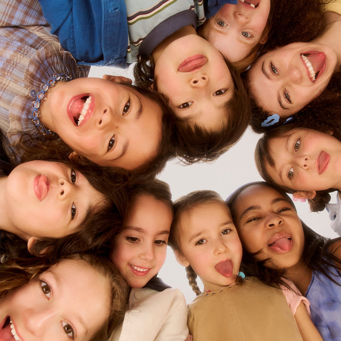 Group of diverse children's faces arranged in a circle looking down at camera, smiling and making playful expressions