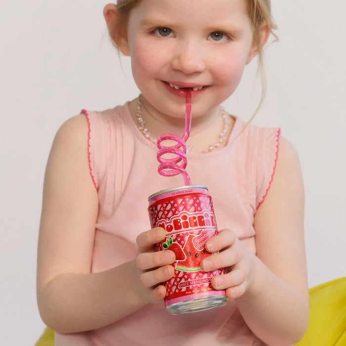 Young girl in pink dress drinking from red "Beehive" sparkling drink can with pink curly straw and pearl necklace